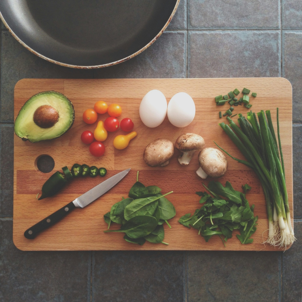 A wooden cutting board with fresh vegetables, eggs, and a knife, ready for cooking.
