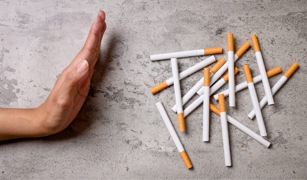 A hand gesturing to stop with scattered cigarettes on a table, symbolizing quitting smoking.