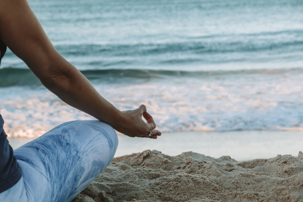 A person meditating on a beach, with the ocean waves in the background.